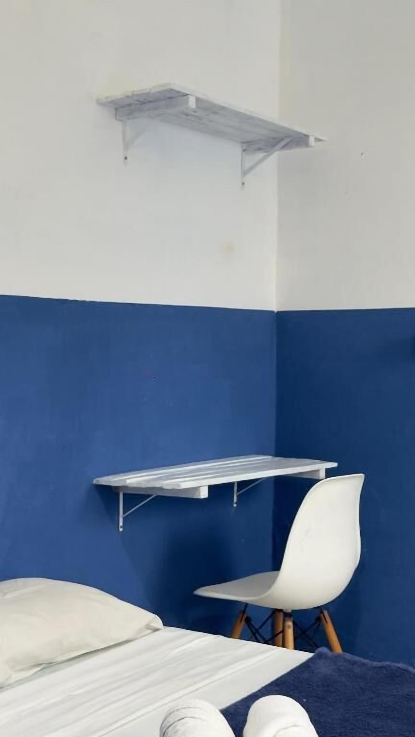 Ein Zimmer mit einem Bett, einem Sessel, einem Regal und einer zweifarbigen Wand.