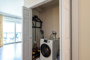A laundry room with a front-loading washer and dryer, a broom, and a vacuum cleaner on a shelf. - Large 2 Bed 2 Bath Condo in Prime West Knoxville/Bearden/Sequoyah Hills (Knoxville)