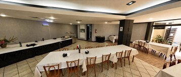 Uma sala de conferências com mesas compridas, cadeiras, uma copa e uma pequena vista para um jardim.