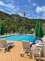 Una piscina con lettini e ombrelloni, immersa nel verde e con uno sfondo collinare.