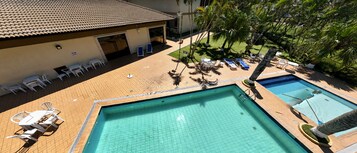 Área de piscina no terraço com duas piscinas, espreguiçadeiras e um espaço de estar coberto.