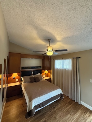 A hotel room with a bed, wooden headboard, bedside lamps, a ceiling fan, and a window with curtains. - Heron Bay 2B 2B condo vaulted ceiling next to pool pwc boat slip available (Osage Beach)