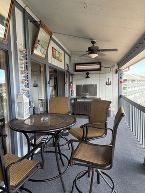 A covered outdoor seating area with a round table and four chairs, a ceiling fan, and a view of the cityscape. - Heron Bay 2B 2B condo vaulted ceiling next to pool pwc boat slip available (Osage Beach)