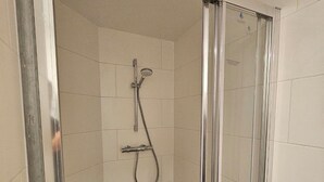 Un área de ducha pequeña y cerrada con puerta de vidrio, cabezal de ducha manual y grifo empotrado.
