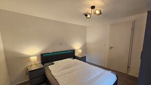 Un dormitorio con cama, mesitas de noche, un armario y una lámpara en el techo.