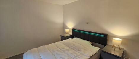 Un dormitorio con cama, mesitas de noche y una lámpara en el techo.