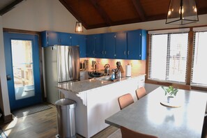 A modern kitchen with blue cabinets, stainless steel appliances, and a large island with seating. - Ski in Style @ Sapphire Squirrel (Wintergreen Resort)