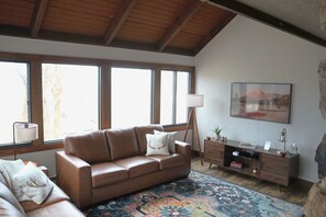 A living room with a brown leather sofa, a patterned rug, a wooden cabinet, and a painting on the wall. - Ski in Style @ Sapphire Squirrel (Wintergreen Resort)