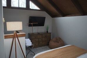 Een slaapkamer met een bed, een dressoir, een televisie, een lamp en een raam.