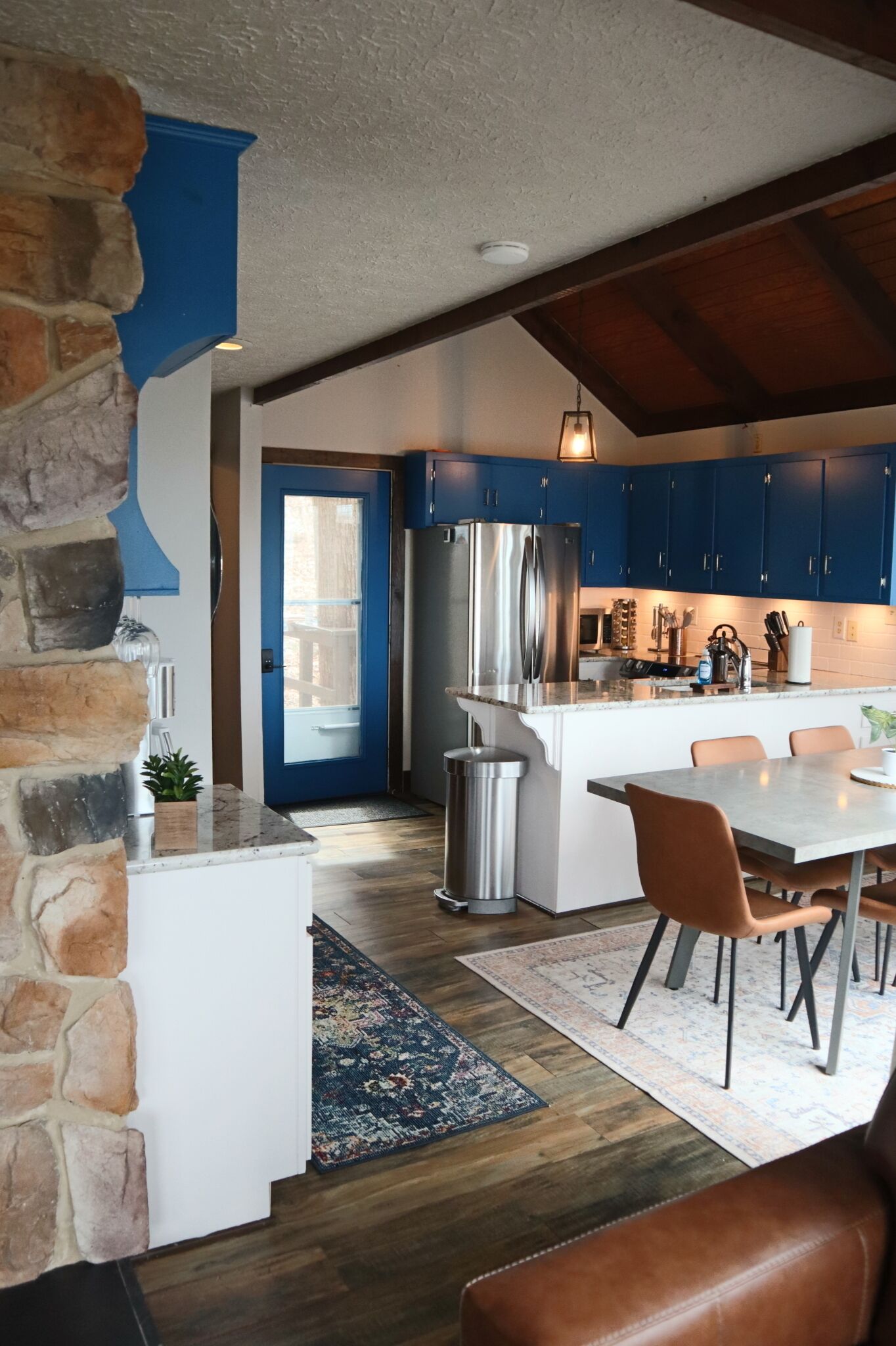 A kitchen with blue cabinets, a stainless steel refrigerator, and a dining area with a table and chairs.