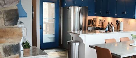 A kitchen with blue cabinets, a stainless steel refrigerator, and a dining area with a table and chairs.