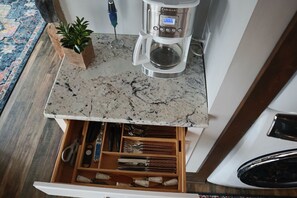 A kitchen with a marble countertop, a coffee maker, and a drawer organizer with utensils. - Ski in Style @ Sapphire Squirrel (Wintergreen Resort)