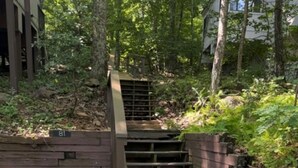 Un escalier en bois avec une rampe métallique menant à un bâtiment, le tout étant entouré d’arbres et de gravier.