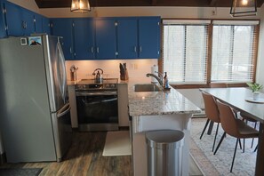 Een keuken met blauwe kastjes, roestvrijstalen apparatuur, een granieten aanrechtblad en een eethoek met stoelen.