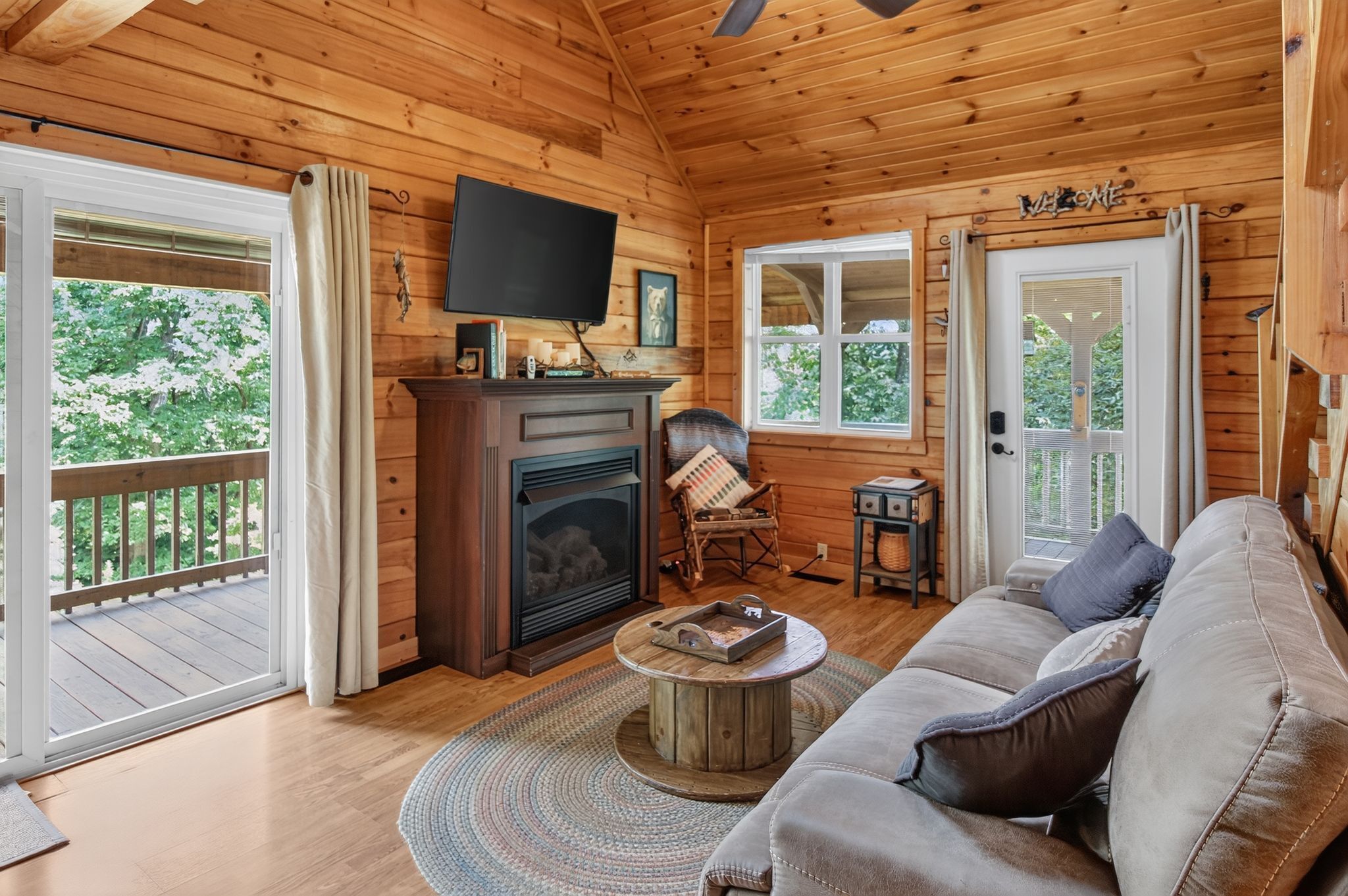 A cozy cabin interior with a fireplace, a television, a sofa, and a view of the outdoors.