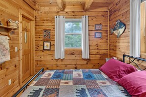 A wooden cabin room with a bed, a window with curtains, and wall decorations. - Secluded Cabin Near Whitewater Rafting + Hiking! (Hartford)