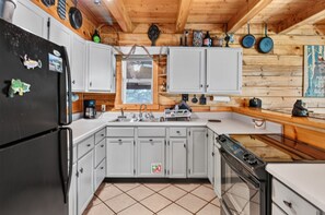 A compact kitchen with white cabinets, a black refrigerator, a sink, and a stove. - Secluded Cabin Near Whitewater Rafting + Hiking! (Hartford)