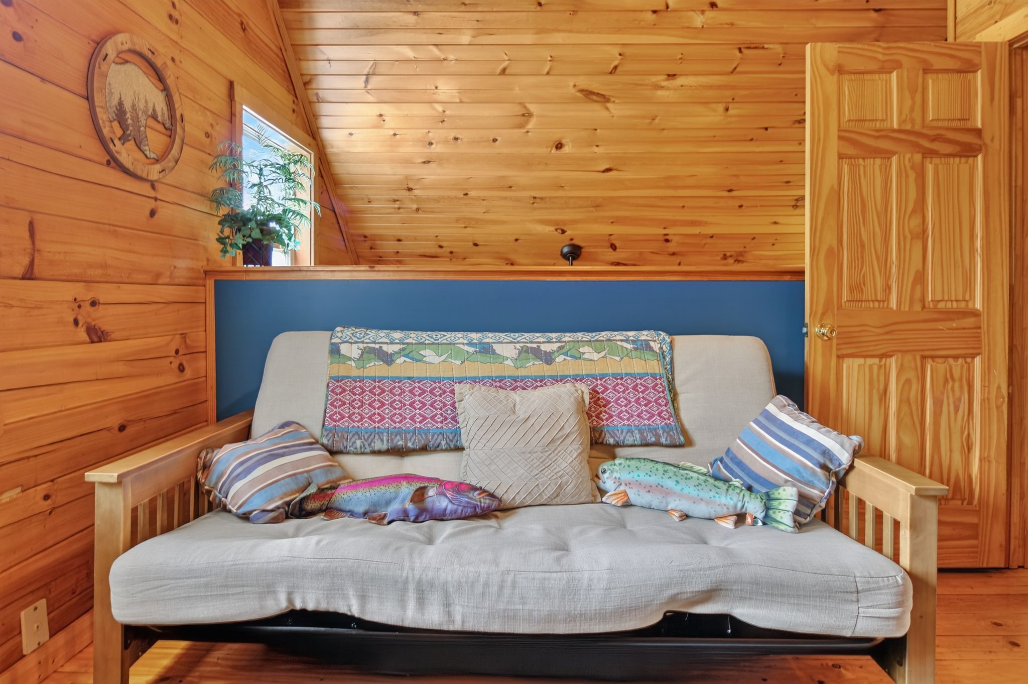 A wooden cabin interior with a sofa bed, pillows, a wall-mounted plant, and a door.