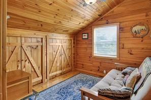 Interior acogedor de una cabaña con paredes de madera, un ventanal grande, un sofá y un aparador de madera.