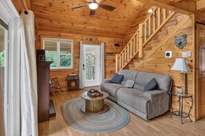 A cozy cabin interior with a wooden ceiling, a grey sofa, a round coffee table, and a staircase. - Secluded Cabin Near Whitewater Rafting + Hiking! (Hartford)