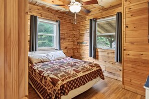 A wooden cabin bedroom with a bed, two windows, and a ceiling fan. - Scenic 4BR Retreat w/ Balcony & Mountain Views (Hartford)