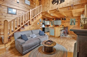 A wooden cabin interior with a sofa, coffee table, kitchen area, and a staircase. - Secluded Cabin Near Whitewater Rafting + Hiking! (Hartford)