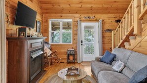 Interior acogedor de una cabaña con chimenea, televisor, sofá y escalera.