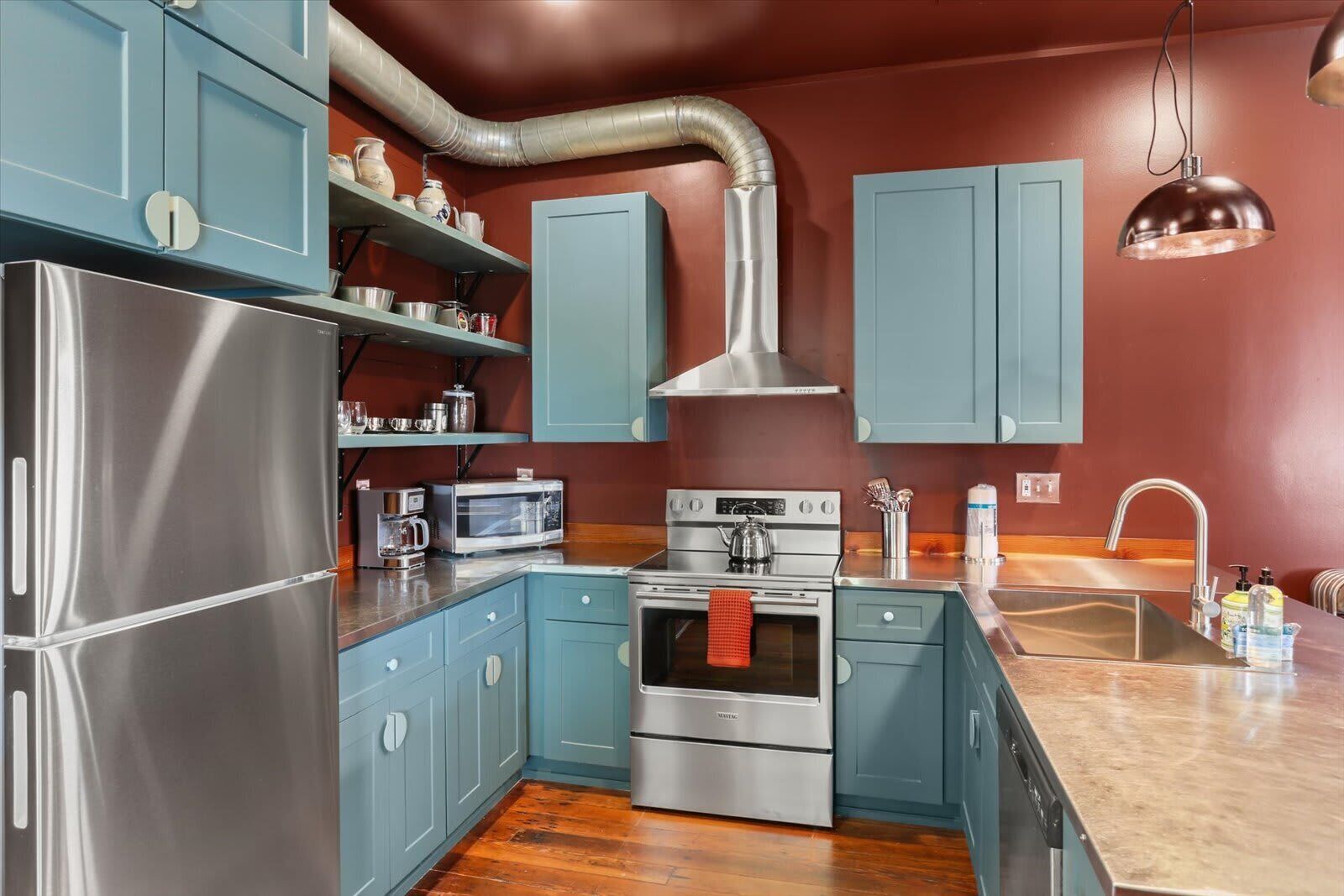 Una cocina con electrodomésticos de acero inoxidable, gabinetes azules y piso de madera.