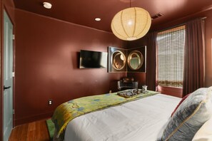 Ein Schlafzimmer mit Bett, Fernseher, Spiegel und einem Fenster mit Vorhängen.