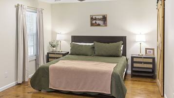 A bedroom with a bed, two bedside tables, a ceiling fan, a window with curtains, and a painting on the wall.