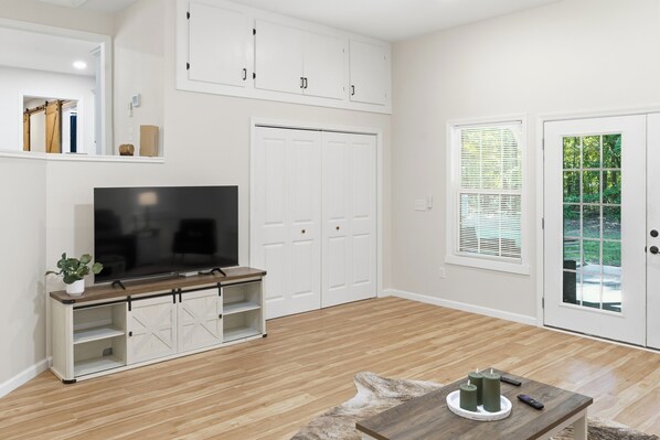 A modern living room with a flat-screen TV, built-in shelving, a sliding door, and a window with blinds.