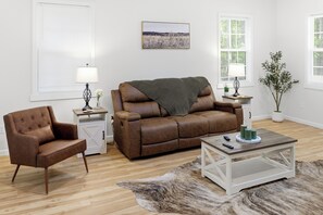 A living room with a brown leather sofa, a leather armchair, a white cabinet, a coffee table, and a shaggy rug.