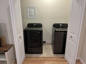 A laundry room with two washers and dryers, wooden flooring, and white walls.