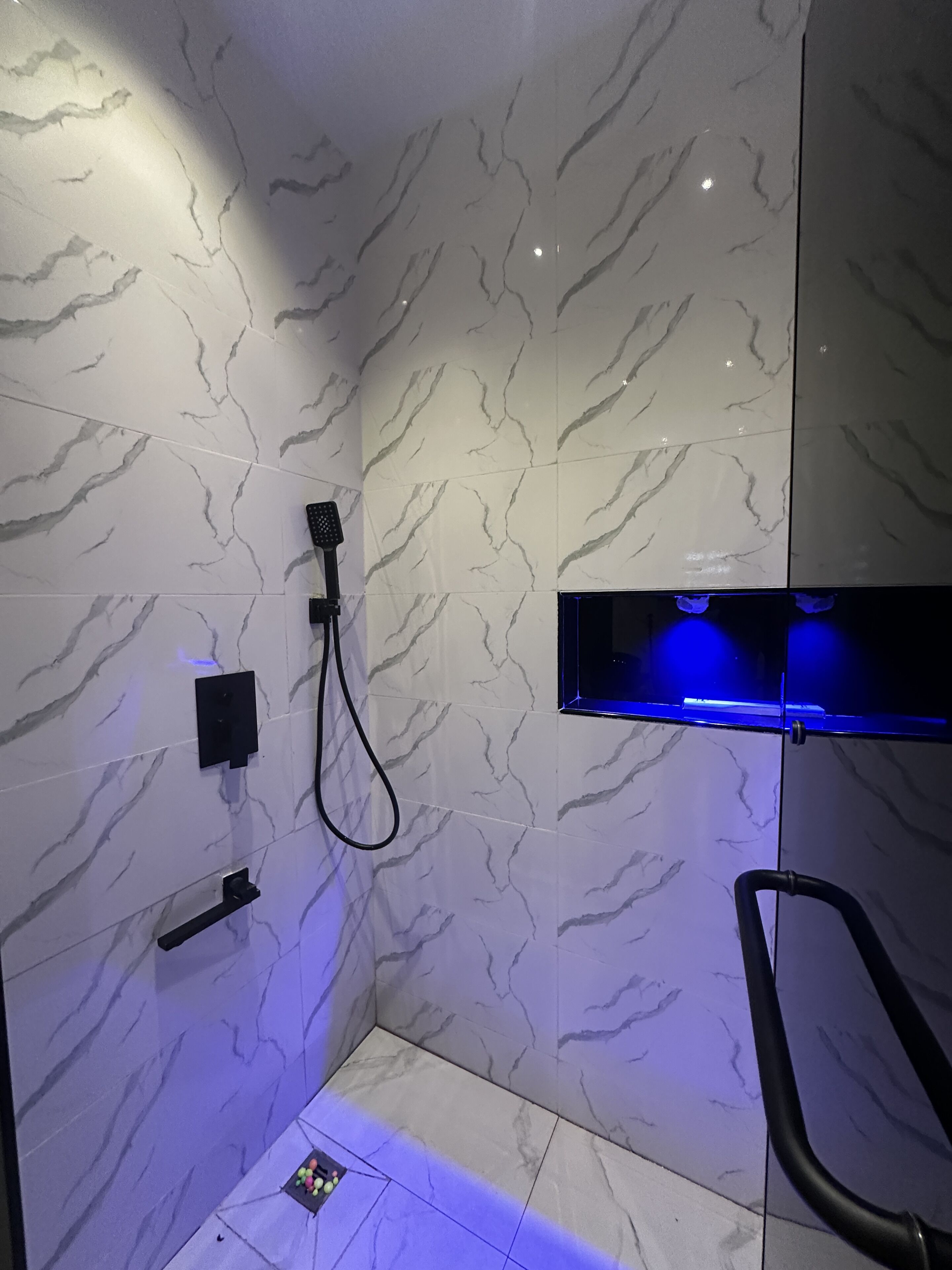 Ein Badezimmer mit Marmorwänden, einer Duschkabine und einem blau beleuchteten Regal.
