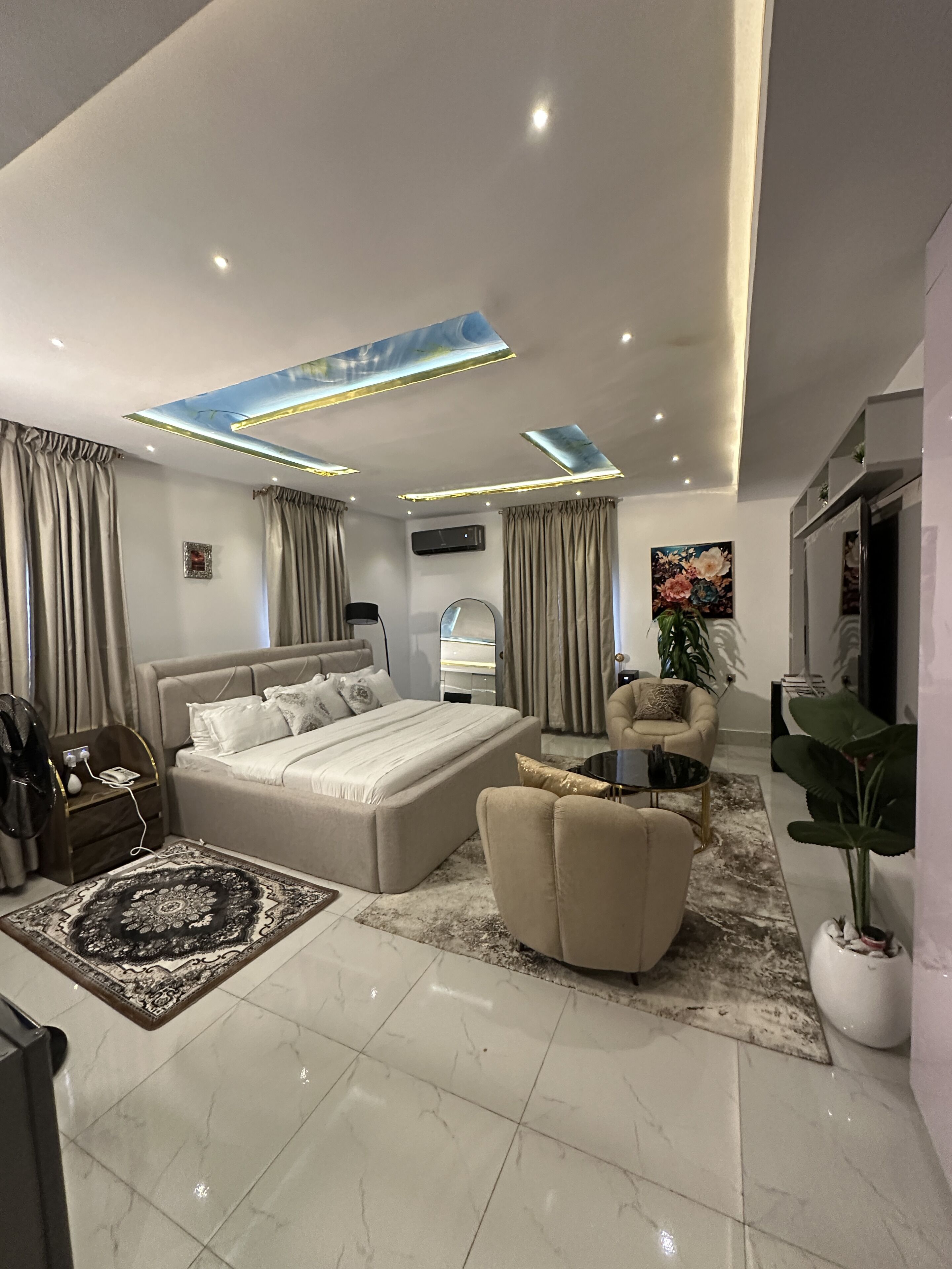 A modern bedroom with a large bed, a seating area, and a dining table.