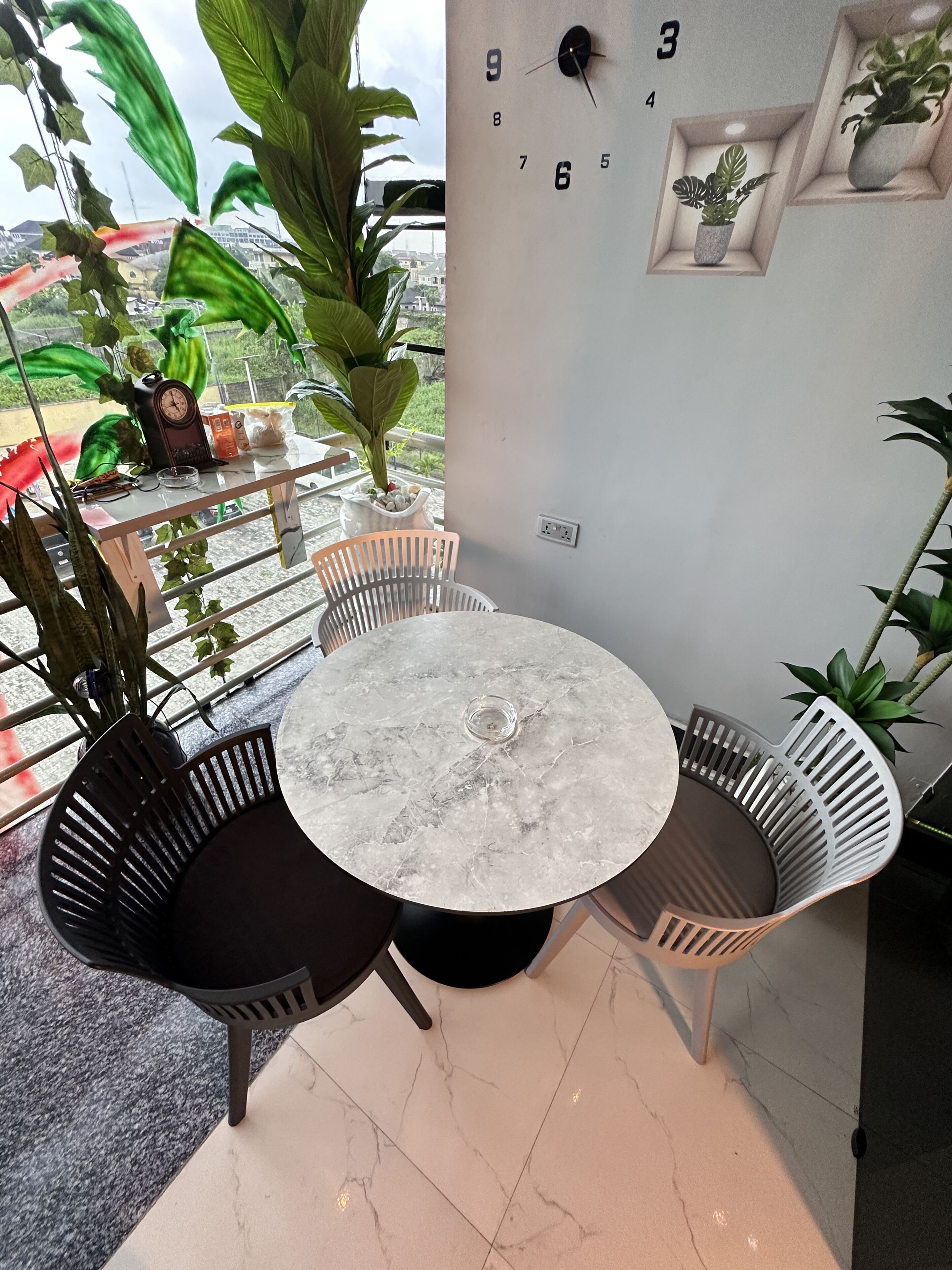 Een ronde tafel met stoelen, een klok en potplanten in een kamer met uitzicht.