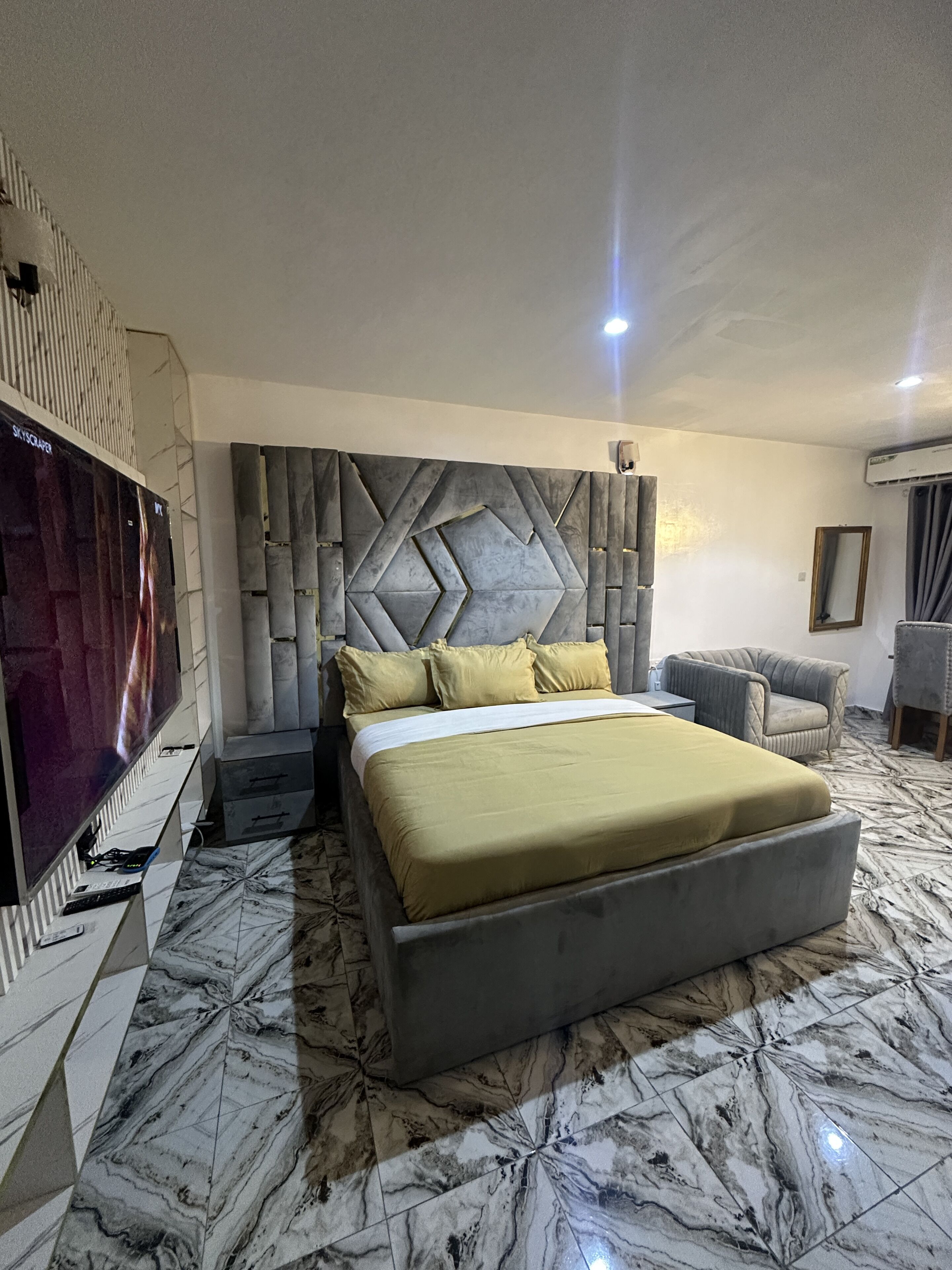 A modern bedroom with a large bed, a television, and a marble floor.