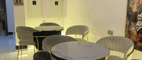 A modern dining area with a round table and six chairs, a wall-mounted control panel, and decorative wall art.
