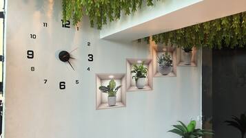 Een muur met een klok, potplanten en een hangende groen decoratie.