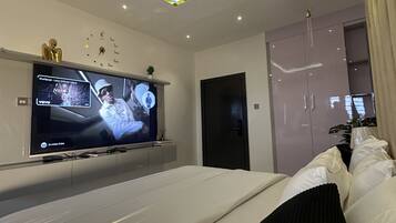 Quarto moderno com cama, televisão e luminária no teto.