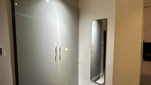 Habitación de hotel moderna con armario de puerta corredera de cristal, un espejo grande y una alfombra estampada.