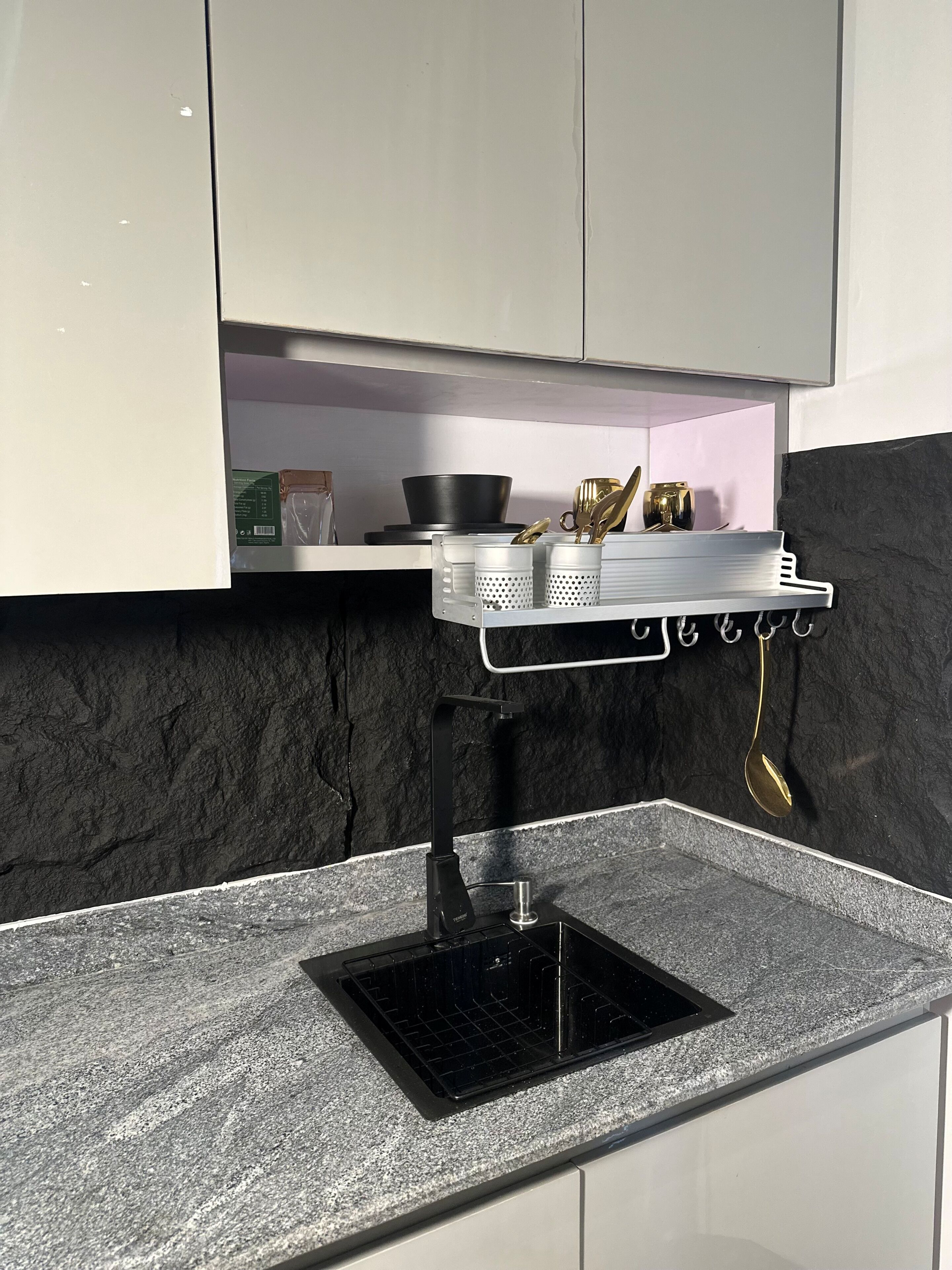 A kitchen with a granite countertop, a black induction cooktop, and a stainless steel rack holding kitchen utensils.
