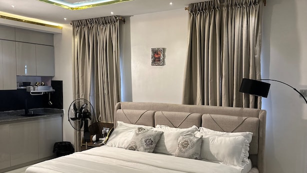 Un dormitorio moderno con una cama grande, una mesita de noche, un ventilador y vistas a una cocina.