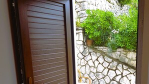 Une porte en bois avec des lattes horizontales, un mur de pierre orné de verdure et un sol carrelé.