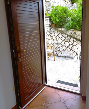 Une porte en bois avec des lattes horizontales, un mur de pierre orné de verdure et un sol carrelé.