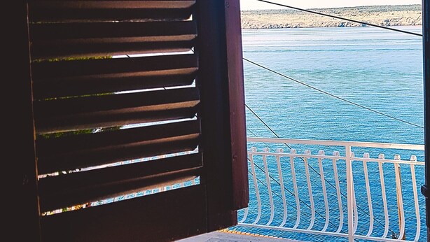 Une vue depuis un balcon doté d’une balustrade, donnant sur une étendue d’eau et une côte lointaine.
