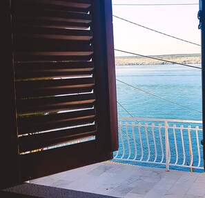 Une vue depuis un balcon doté d’une balustrade, donnant sur une étendue d’eau et une côte lointaine.
