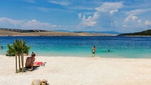 Une plage à l’eau d’un bleu limpide, avec un rivage sablonneux et quelques personnes qui se baignent.