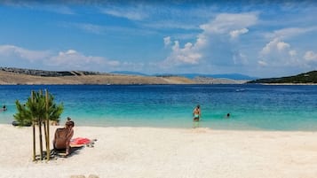 Uma praia com águas azul-claras, areal arenoso e algumas pessoas nadando.