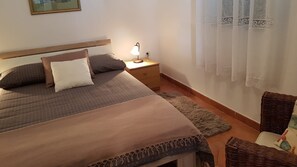 A neatly arranged bedroom with a bed, bedside lamp, and a wicker chair.